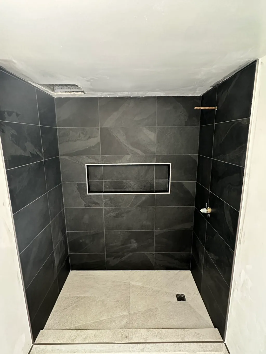 A custom black-tile walk-in shower built by Naron — moody, precise, fully waterproofed.